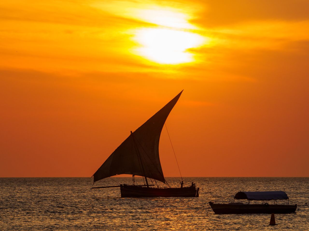 A dhow sailing in silhouette against an orange sunset off Zanzibar