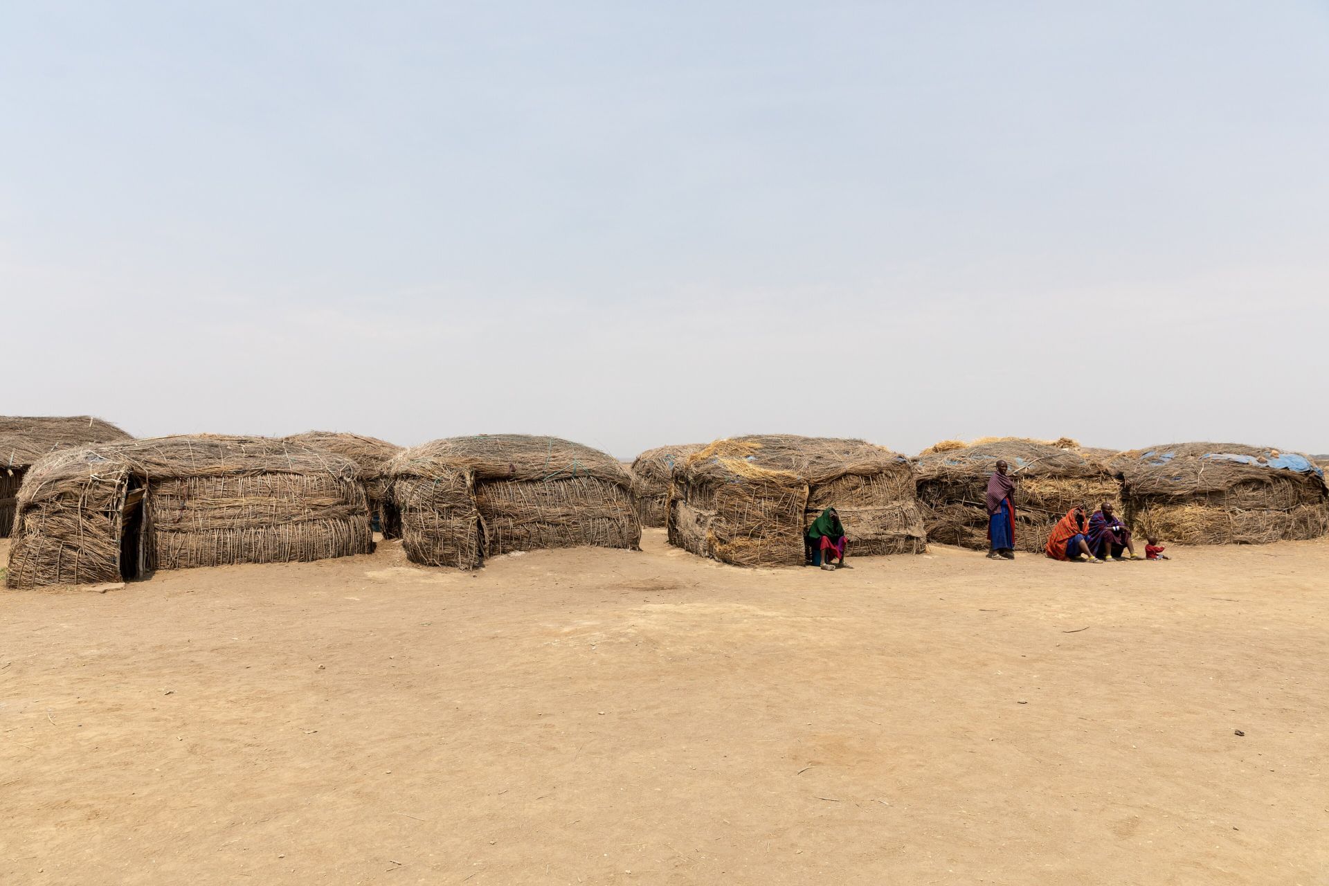 Low mud houses of a Maasai homestead on bare dry ground
