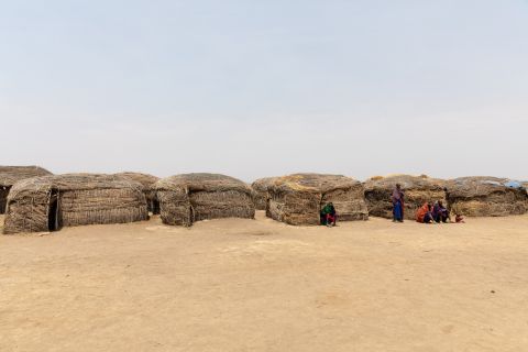 Low mud houses of a Maasai homestead on bare dry ground