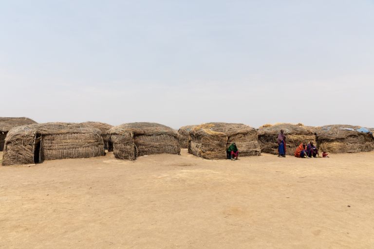 Low mud houses of a Maasai homestead on bare dry ground