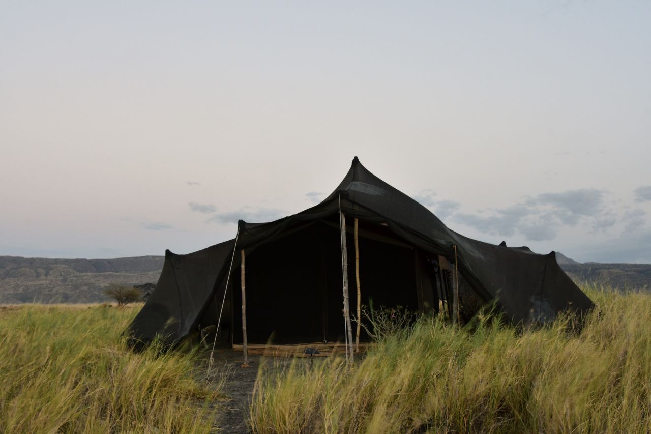 A canvas safari tent standing in grassland in evening light